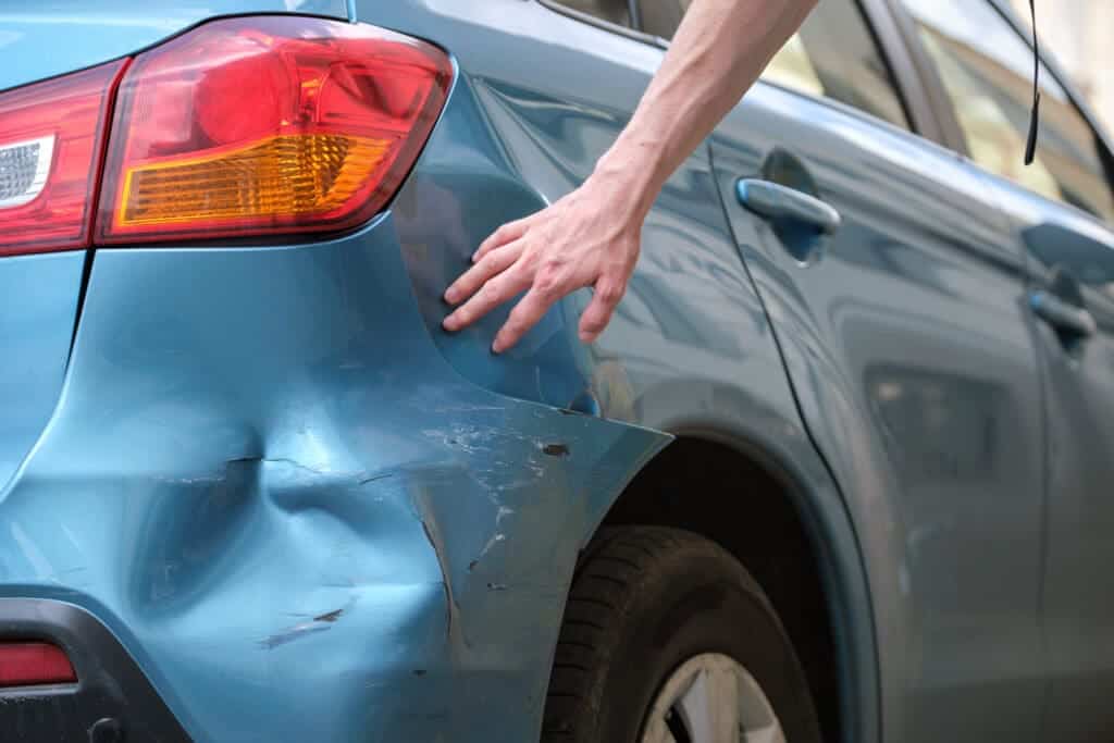 Driver hand examining dented car 