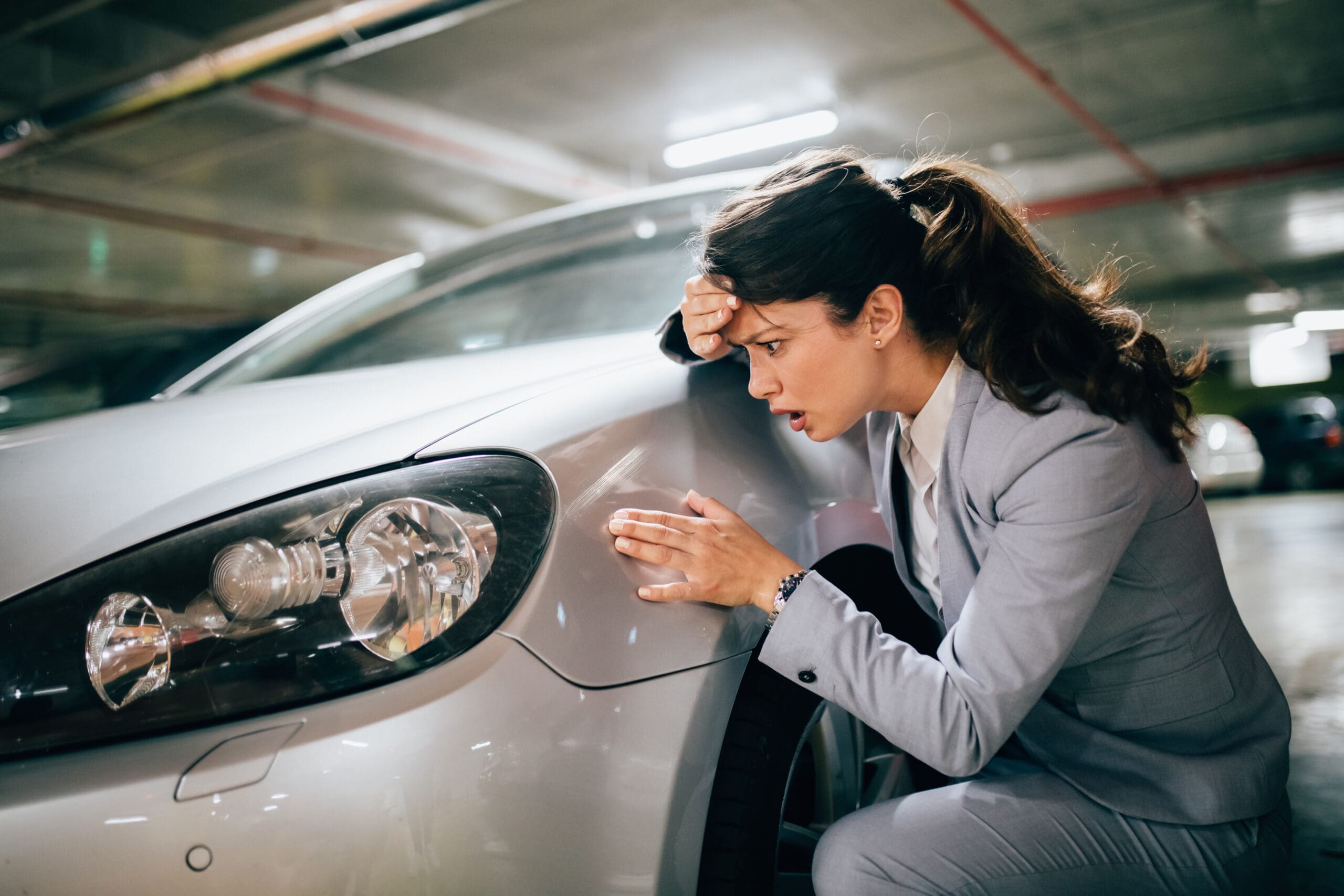 Young woman inspecting damage to parked car